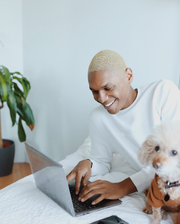 A person types on their laptop with their small dog