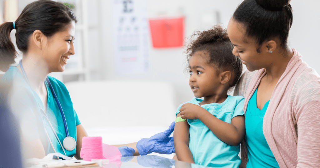 Person holding child who just got vaccinated, looking happily at nurse
