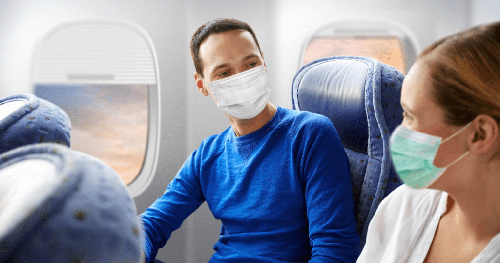 Two people on airplane wearing masks sitting side by side looking at each other