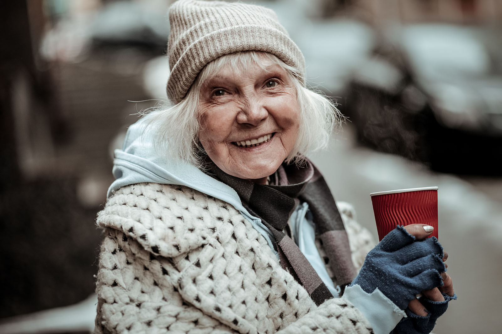 A senior woman similng and holding a coffee cup outside