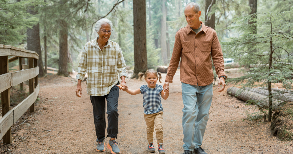 Two older adults with their grandchild walking through a park holding hands
